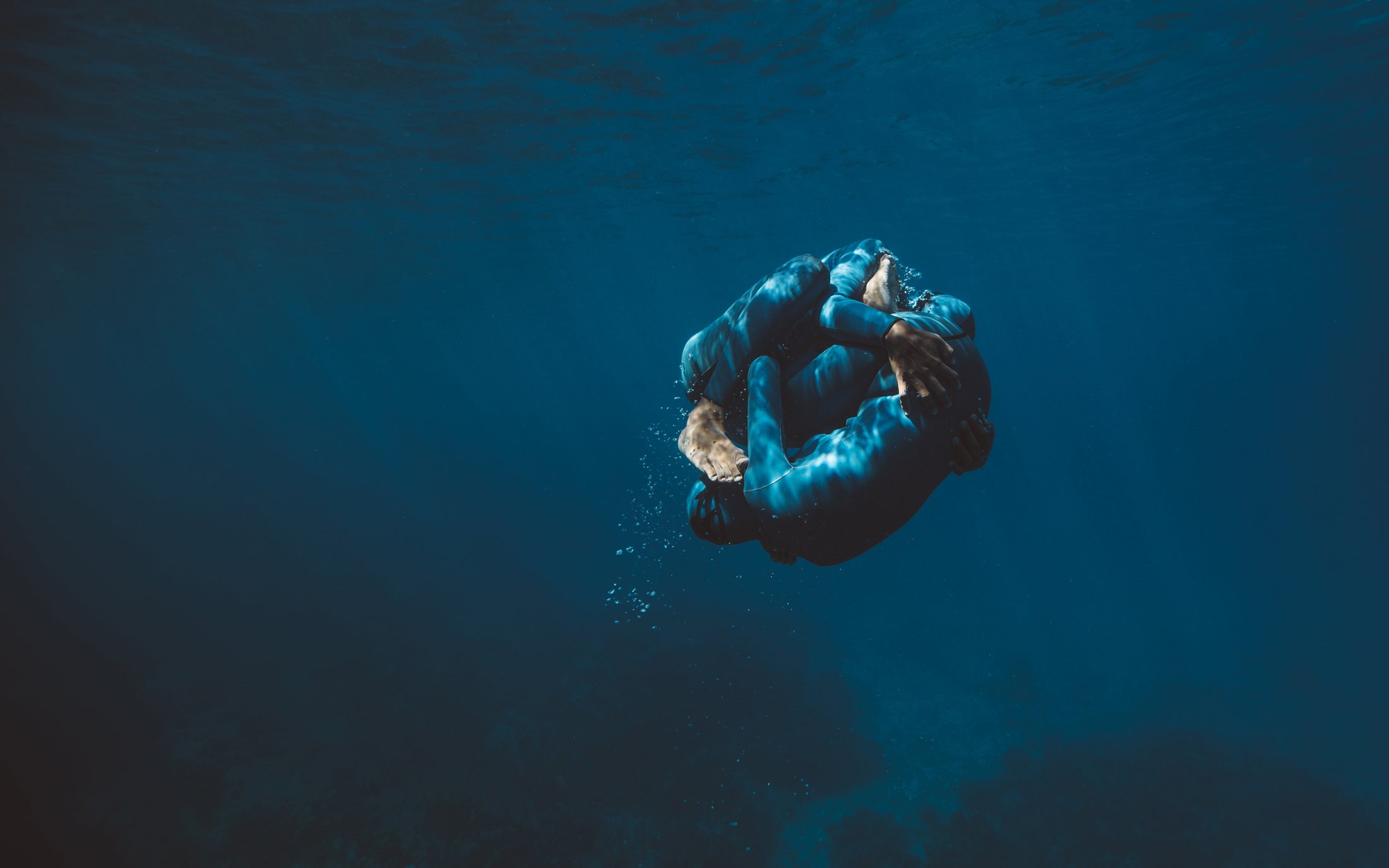 Dos cuerpos pintados de azul enroscados en una esfera bajo el agua
