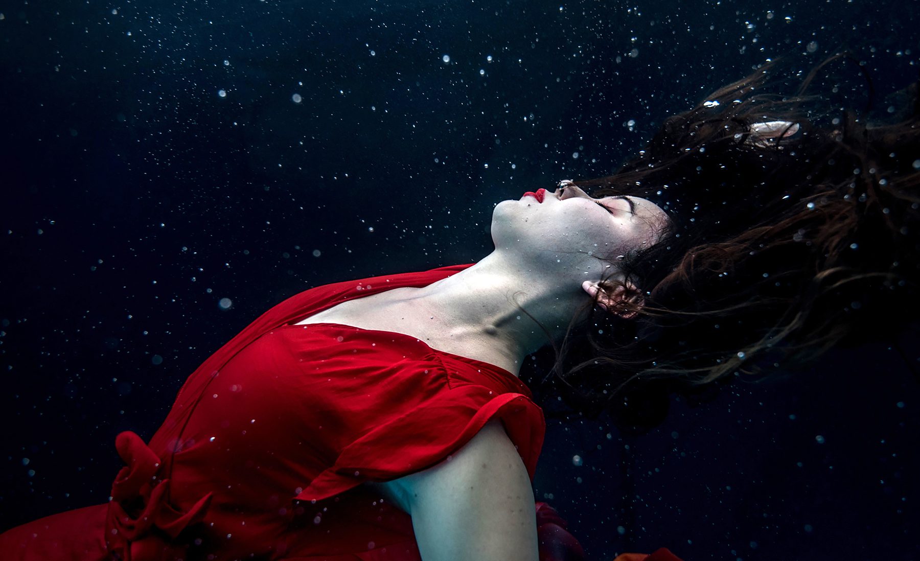 Una mujer con una tela roja flotando bajo el agua